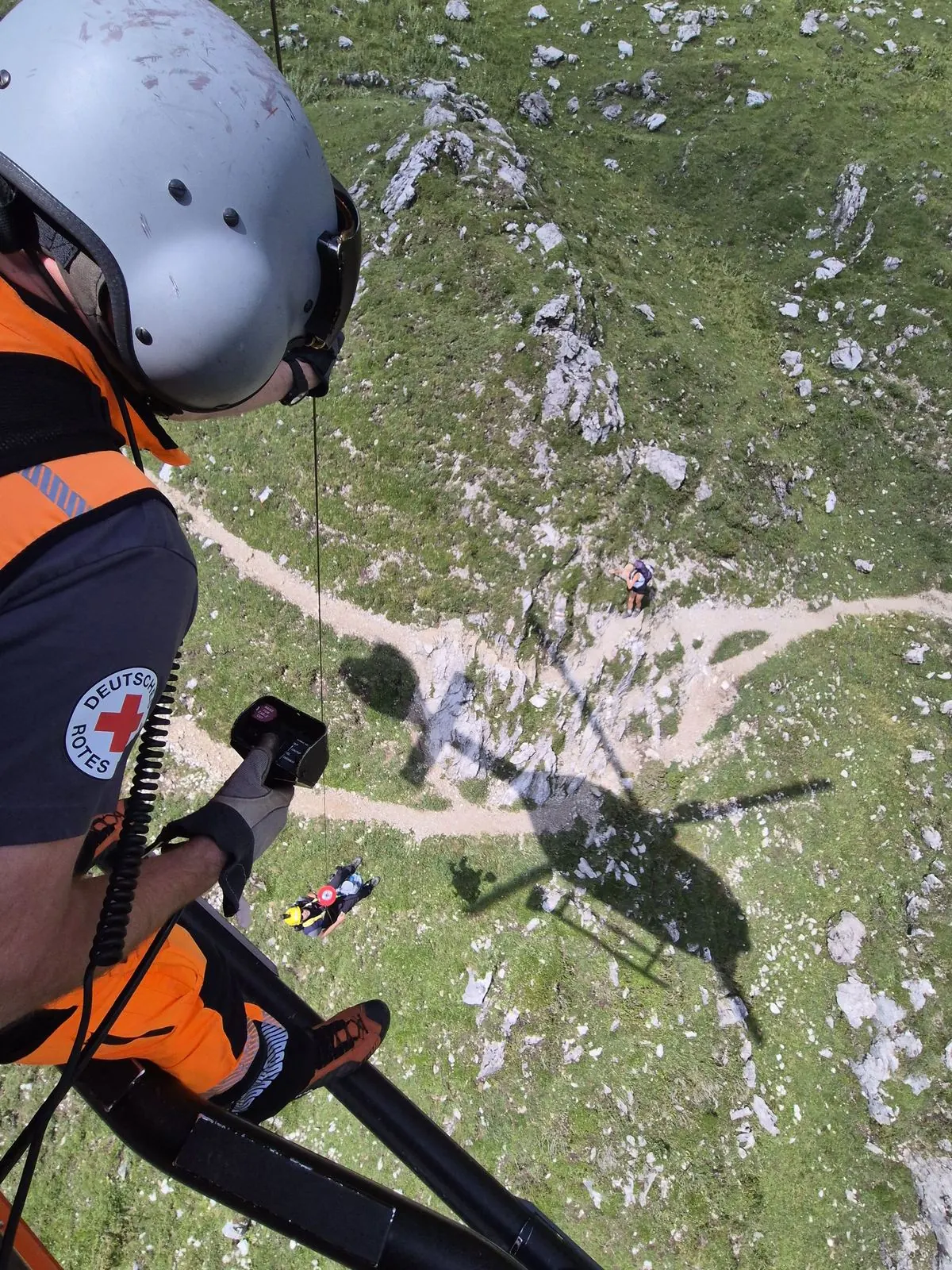 Blick aus der Kabine nach unten auf einen Bergweg, Windenoperator an der Tür